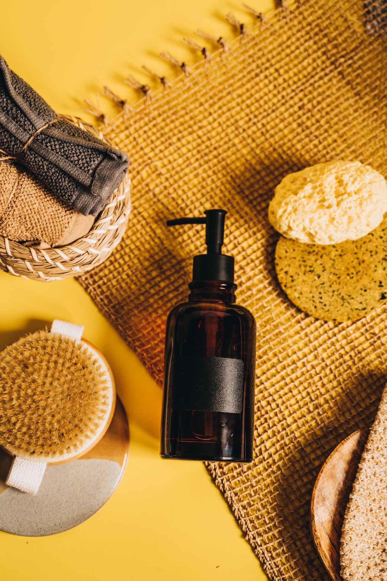 Flat lay of spa essentials including a pump bottle and exfoliating brushes on a woven mat